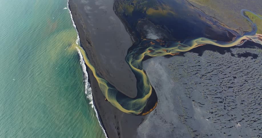 Aerial of a colorful river on the black sand beach
