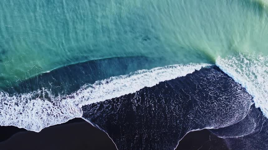 Aerial of a blue sea wave on the black beach