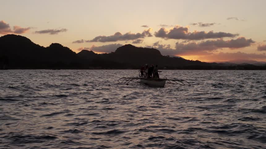 A small boat is in rough waters at sunset