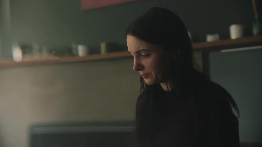 A woman in a black shirt is sitting with worried looks while looking at papers in her hands
