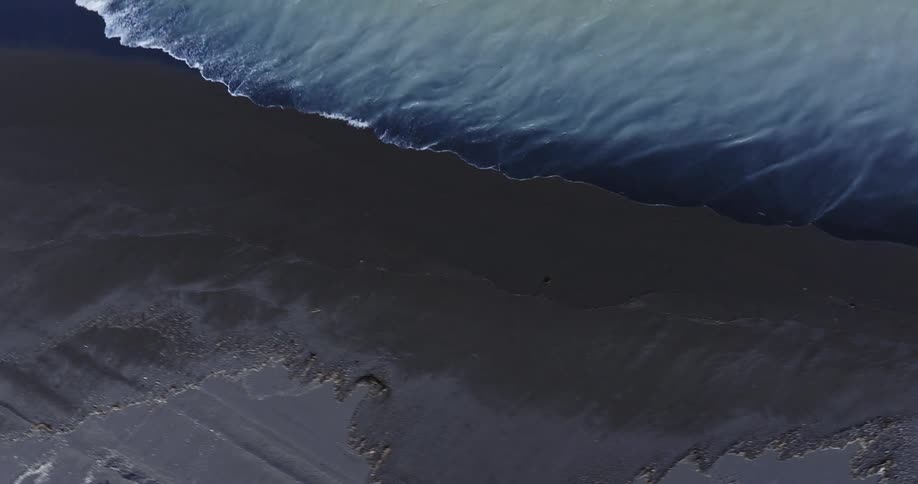 Clear water waves roll into shore and over the black beach