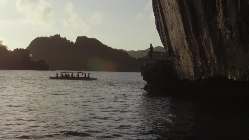 Person on rock ledge looks at a boat full of people