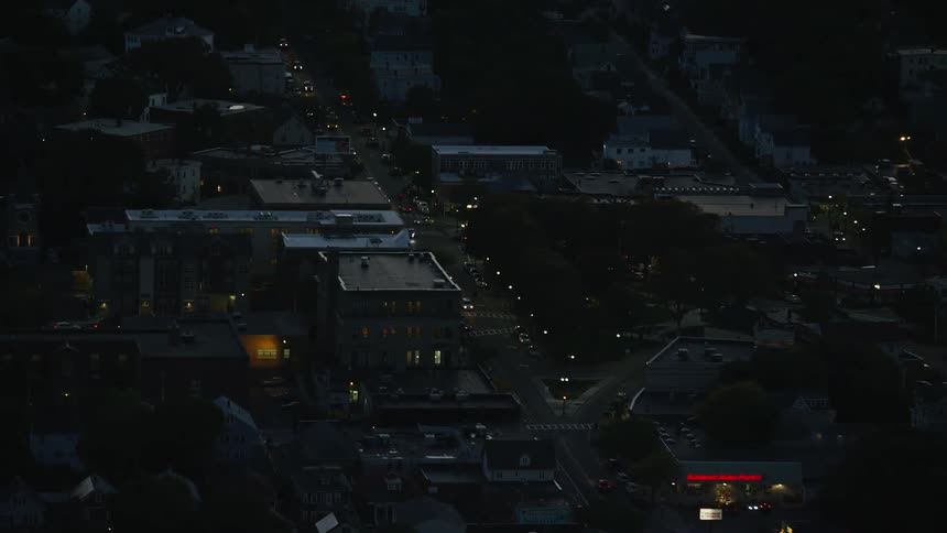 Heavy traffic flows along city street passing low rise buildings at night