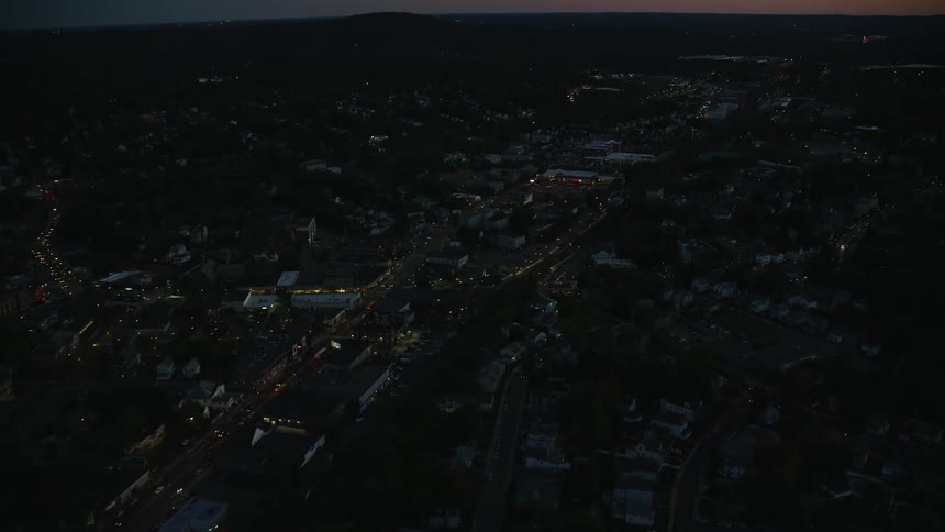 A region of a city with few houses and several trees in the middle and everything is dark according to the night