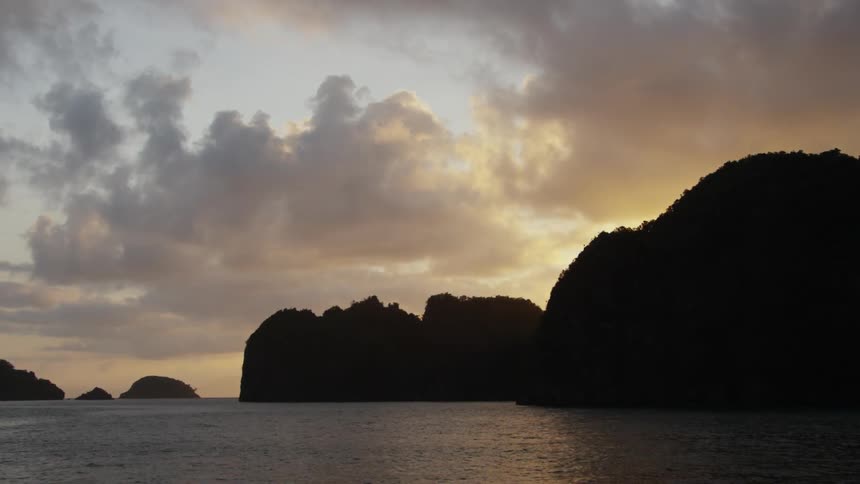 The sun setting behind ocean cliffs on a cloudy evening