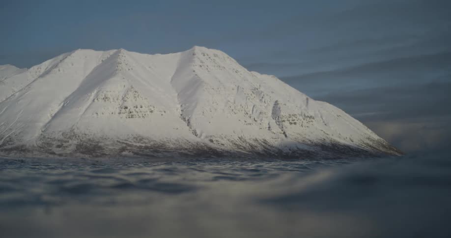 Panorama from inside the sea with calm waves and a snowcovered mountain in the distance
