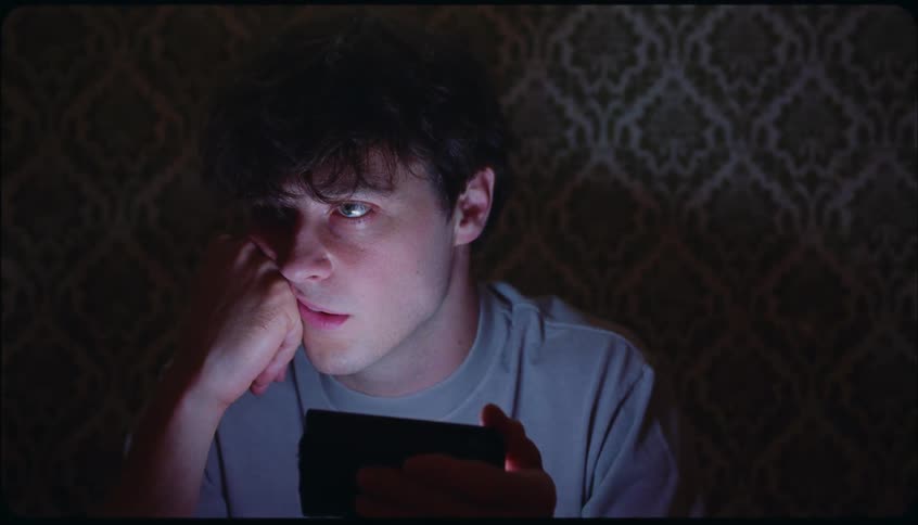 Frowning man glances at smartphone in dark room