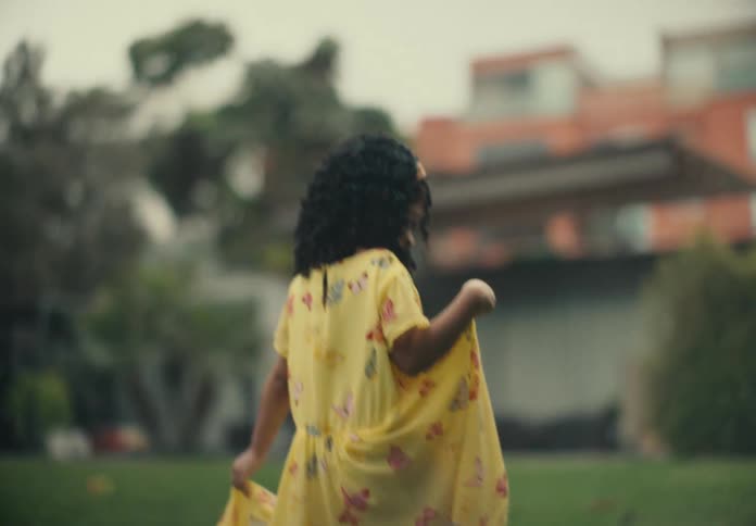Young girl walking in a backyard wearing a yellow dress