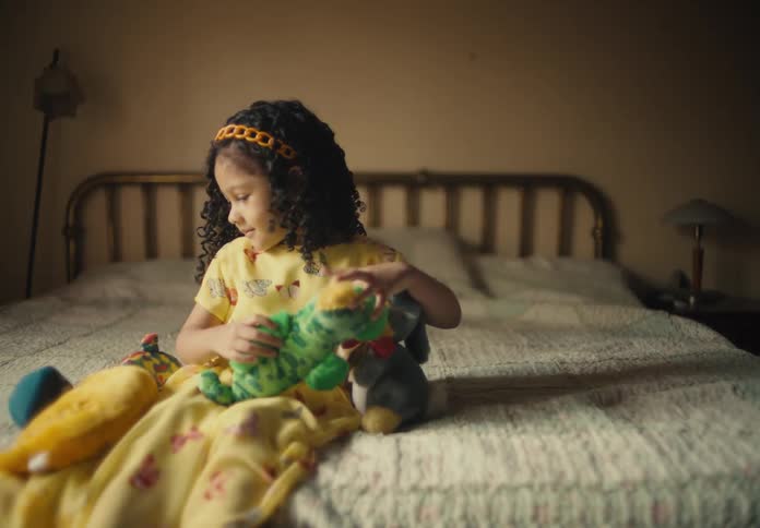 A child playing with her stuffed animals while sitting on a bed indoor