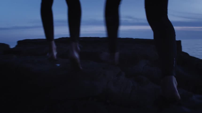 Two people walking barefooted on a cliff by the sea at dawn
