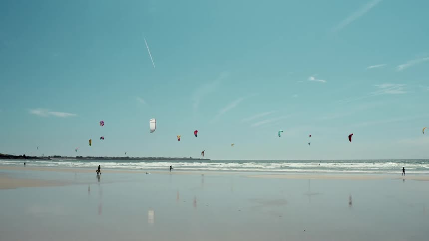 Surfers kite fliers and kite surfers share wide beach on slightly cloudy day