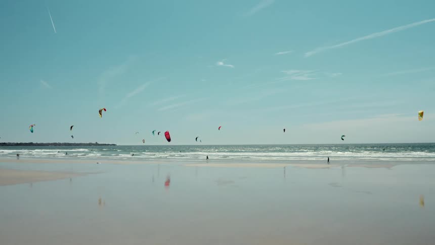 People fly kites on the beach under contrails and small clouds