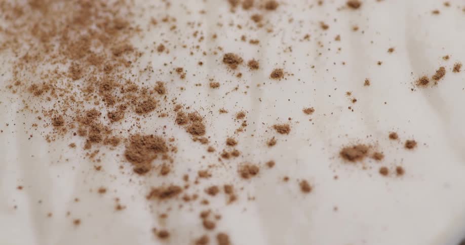 Cocoa powder being sprinkled onto a white cream dessert