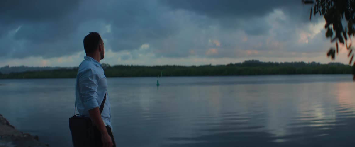 A man stands at the edge of the lake watching the sunset