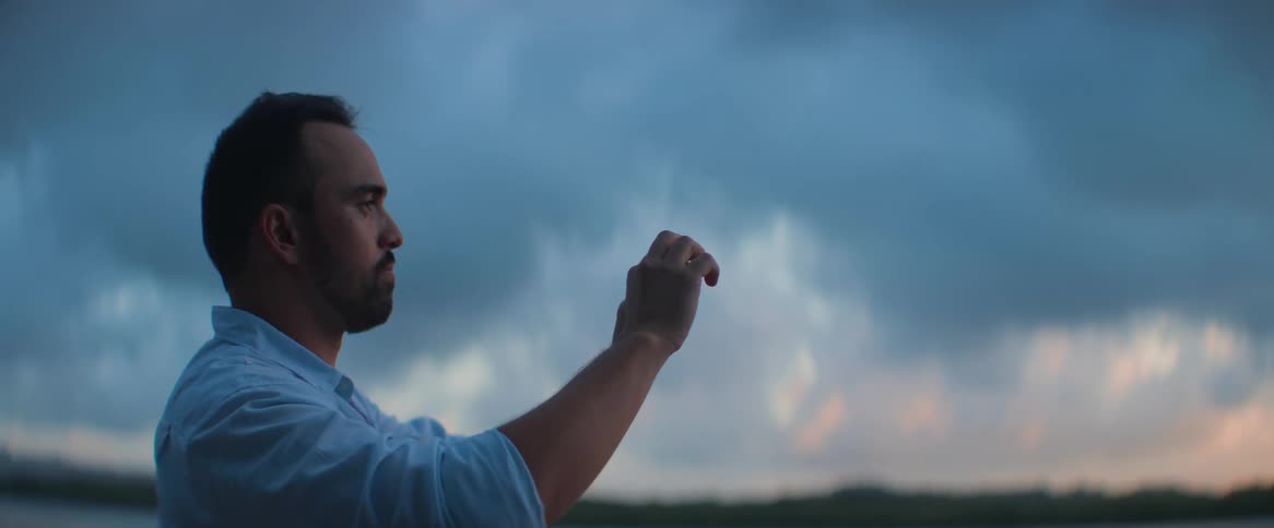 A man recording the landscape of a lake and a dawn sky with his cell phone
