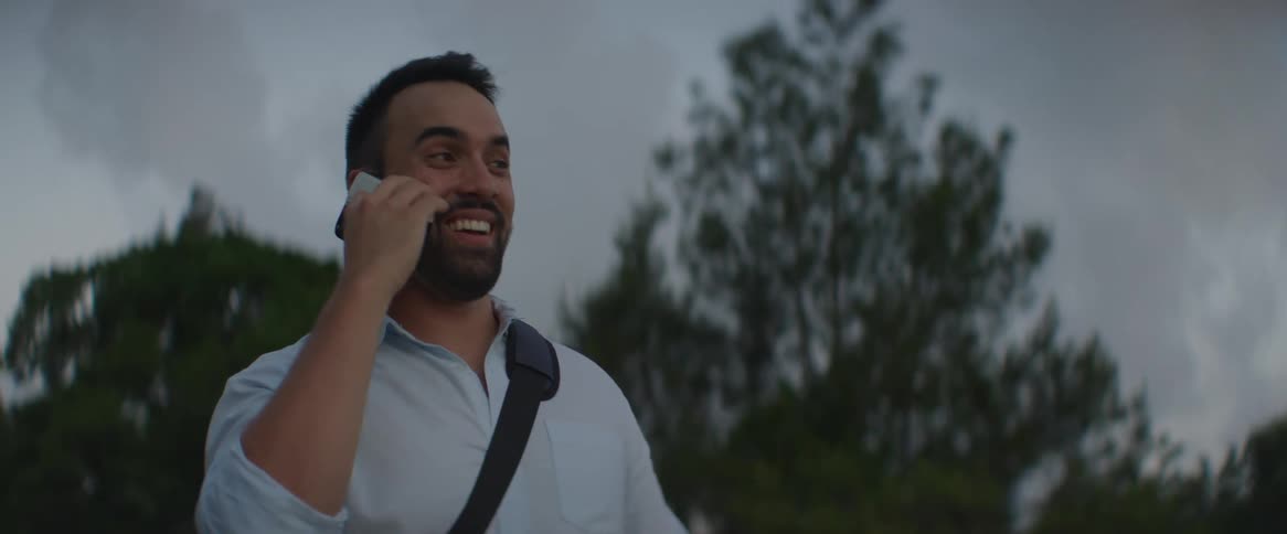 A man smiling while talking on phone at sunset