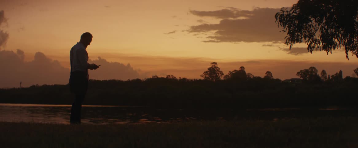 A man reading by the river at dusk