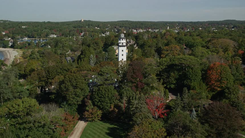 Lighthouse towers over wooded coastal neighborhood surrounding marina