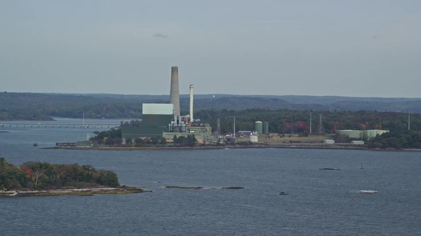 An tower of a factory that faces the sea with a a little island on front
