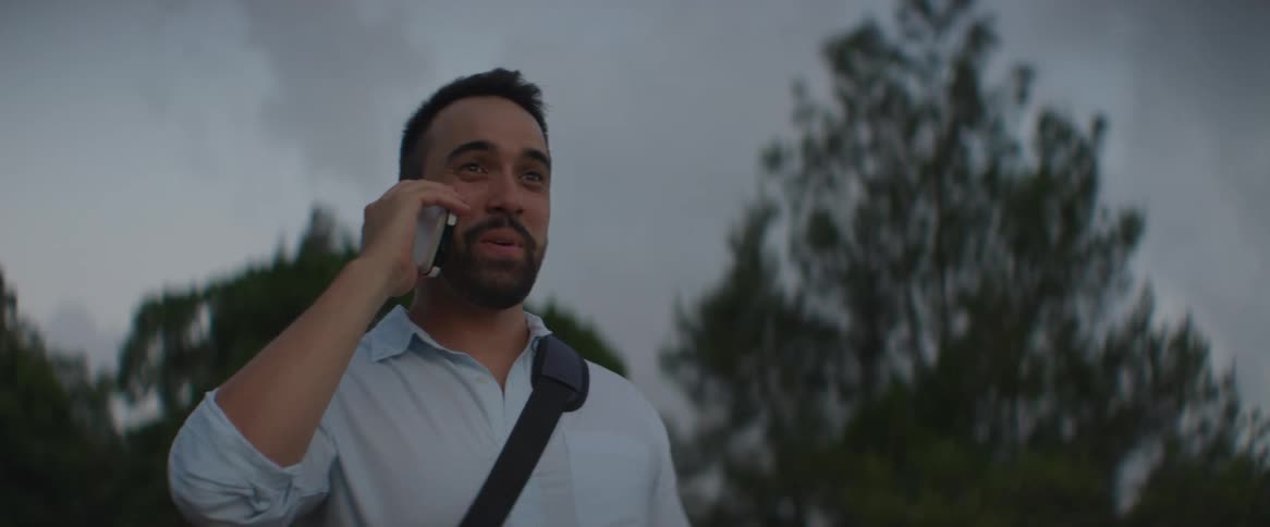 Smiling man talking on the phone in an outdoor setting with a cloudy sky