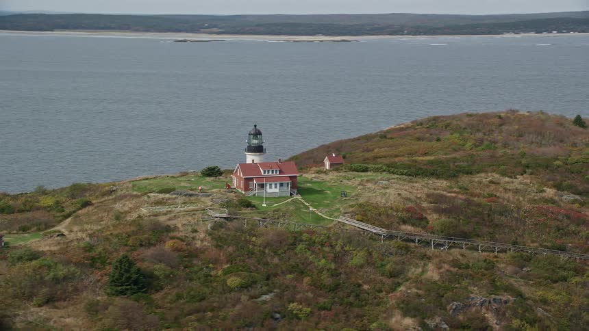 Aerial of a house and a lighthouse high on a mountainous island