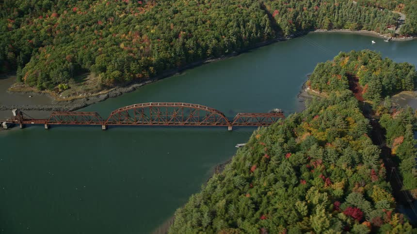 An aerial view of a bridge linking the end of two river banks in the woods