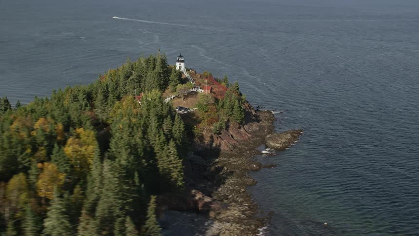 An island filed with trees with a building and a light house close to shore
