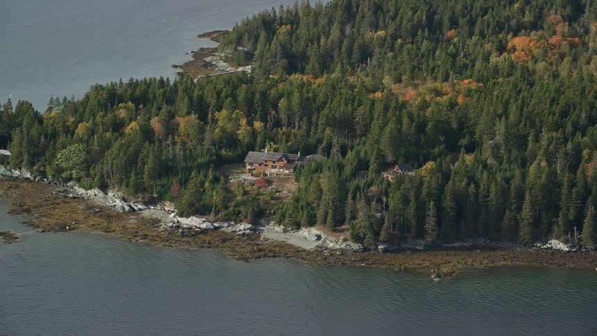 An aerial shot of a building in a forest on the coast