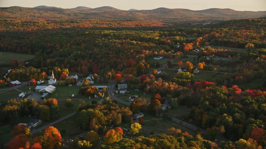A rural region with some houses in the middle of forests of trees that are changing color due to the season