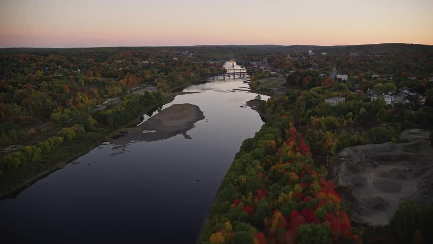 A reflective river amidst forests and behind a rural area with houses