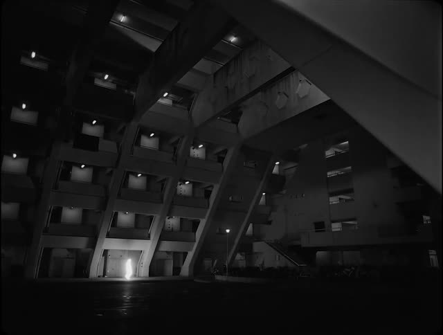 A luminous shape walking through the courtyard of a building at night