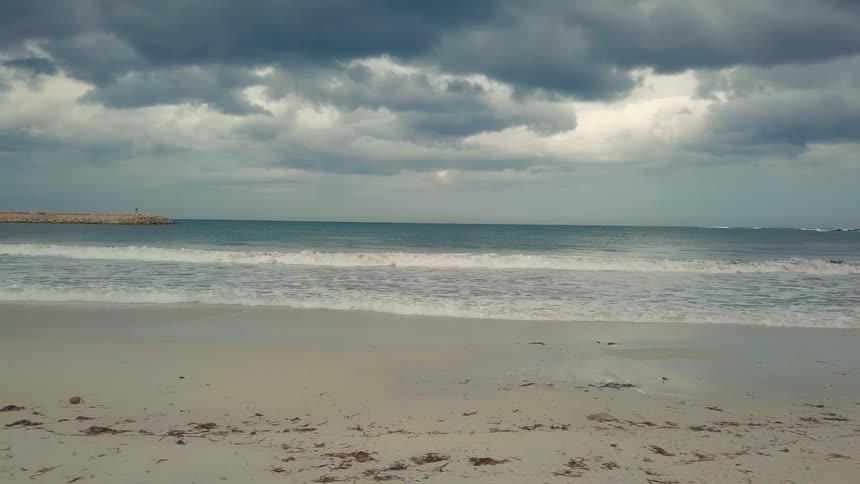 Waves splash as they roll into shore and over the beach under a cloudy sky