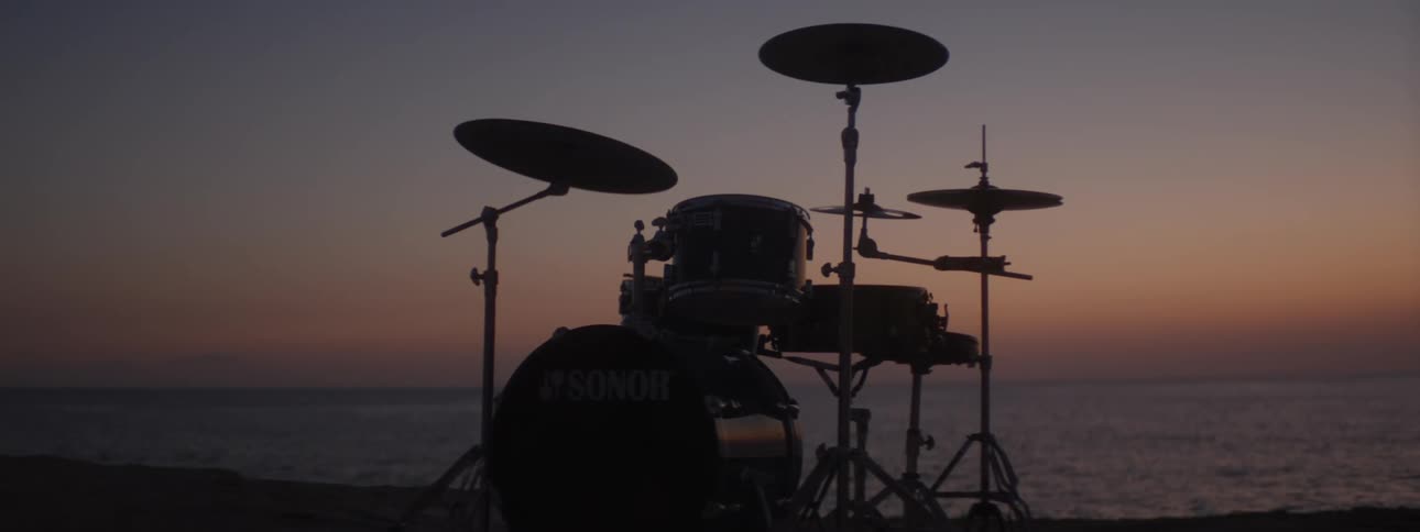 A drum set along the coast is silhouetted as the sun sets