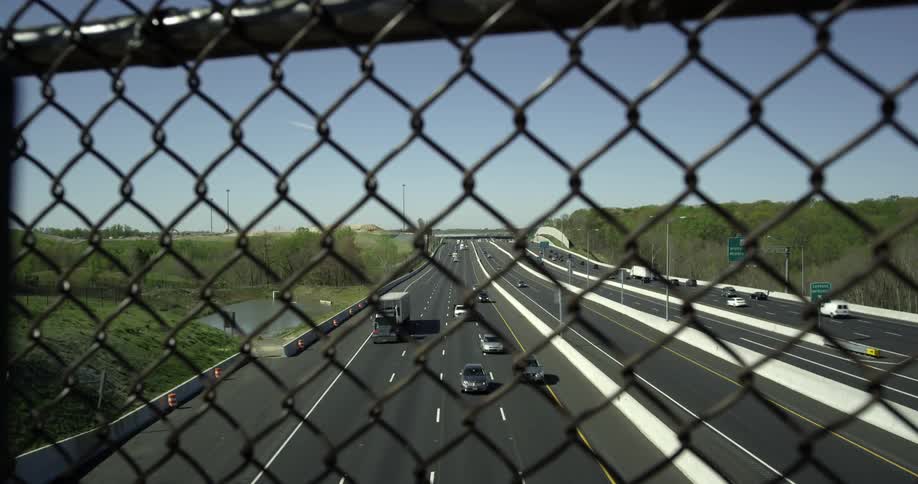 Through the fence of an overpass cars are traveling below