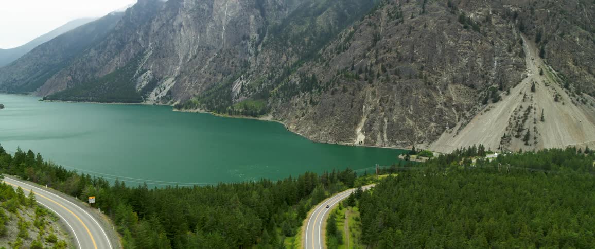 Aerial of the road in the middle of the forest with a lake and mountains