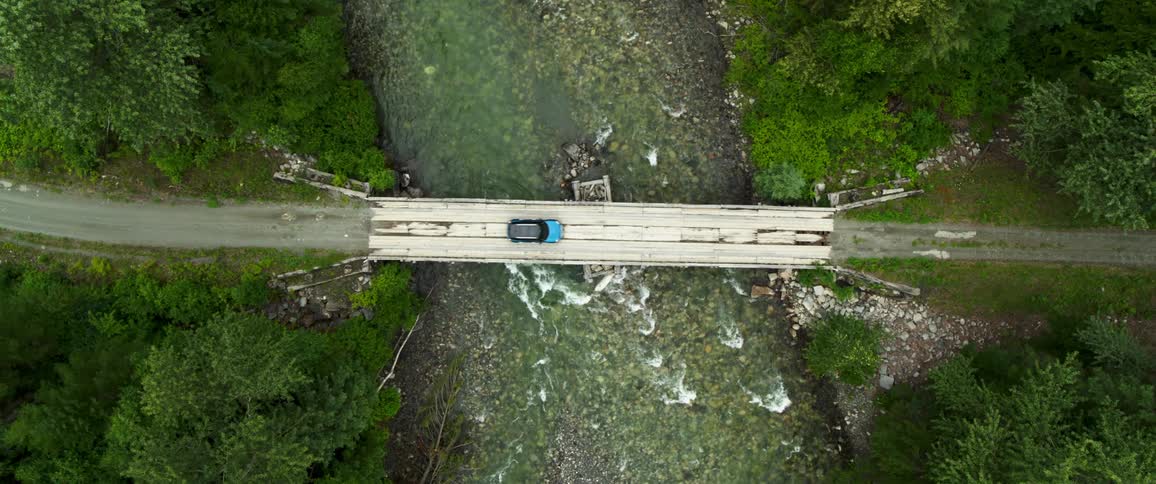 Blue vehicle drives across bridge over river