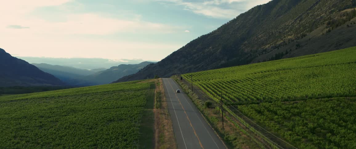 An aerial view of a car driving down a street between plowed fields