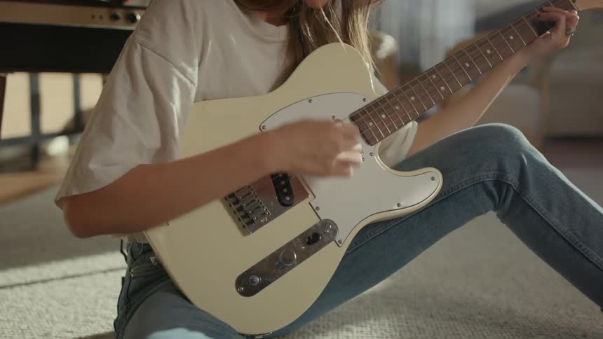 A woman playing guitar on the floor looking at notes on her cell phone