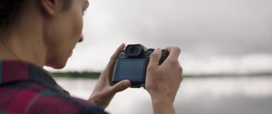 Lady stands near a river and take pictures of the surroundings during the day