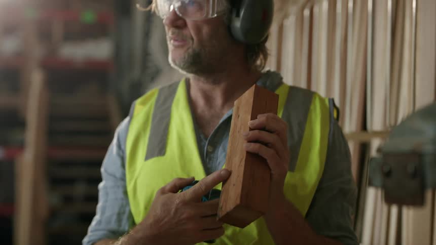 A worker wearing goggles headphones and a safety vest demonstrates a brick to a group of people
