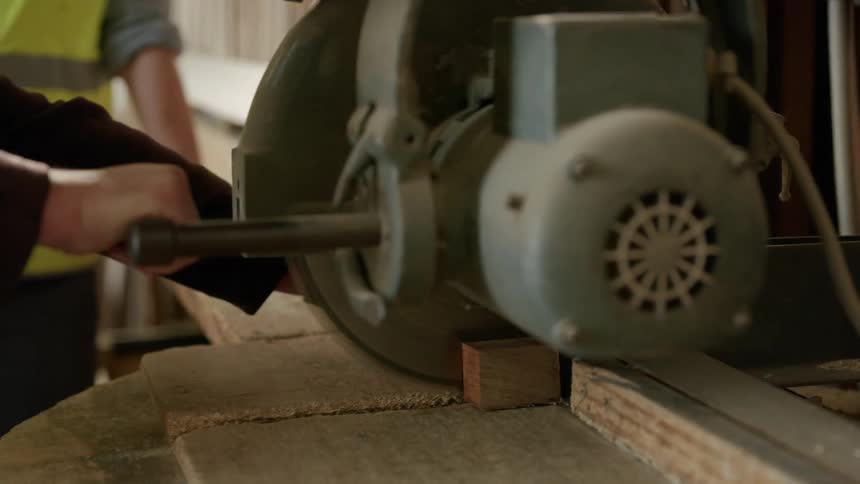 Worker cuts wood with a powered saw as another man watches