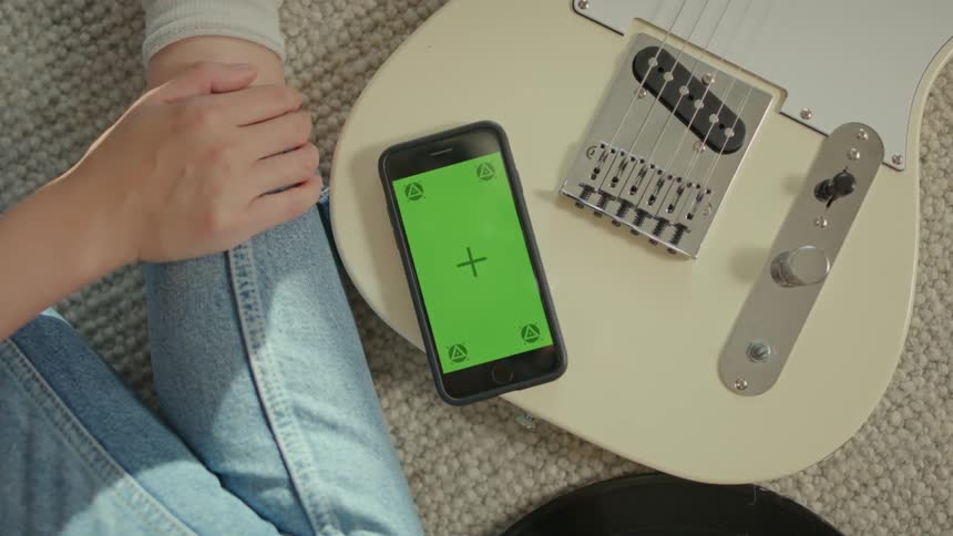 A cell phone with a green screen on top of a guitar