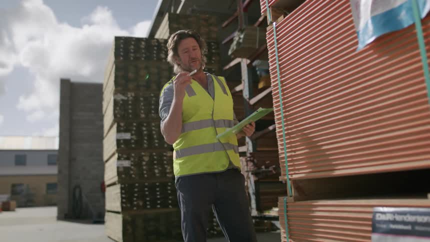 A man checking stacks of wood and jotting down notes in his notebook