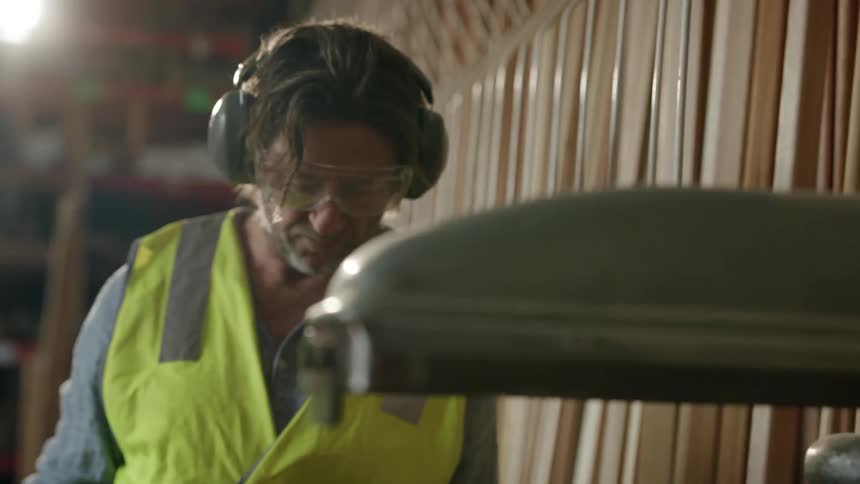 A person wearing personal protective equipment measuring a wooden piece