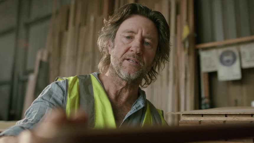 Man wearing safety vest runs hand over carpentry