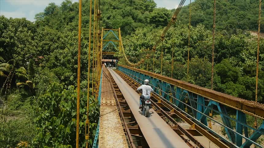 A man is riding a motorcycle over a bridge