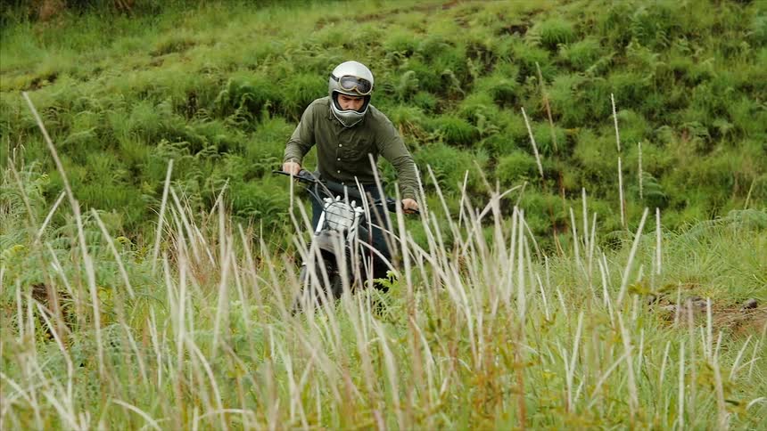 A man is riding a dirt bike up a grassy hill
