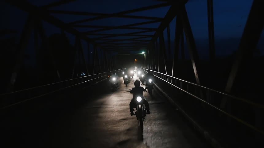 Motorcyclists crossing a bridge at night