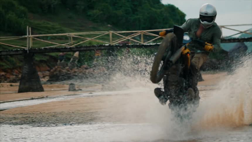 Motorcyclist riding a wheelie through some shallow water