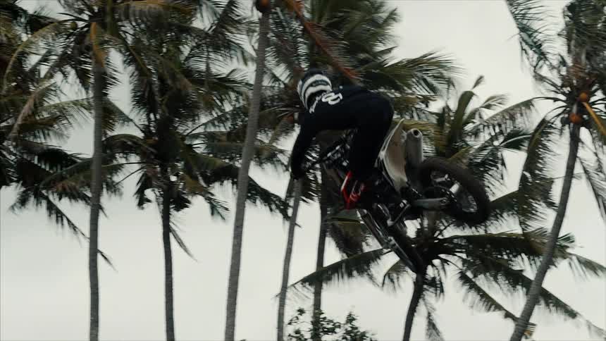 A man in the air on a dirt bike with palm trees